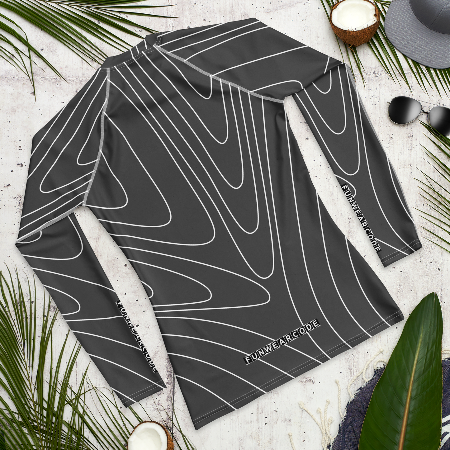 Black and white patterned rash guard with a brand logo 'Funwearcode' on a textured surface with palm leaves and a hat.