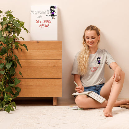 Woman sitting on the floor with a book, wearing a t-shirt with text and a playful lady ninja graphic design, in a room with a wooden dresser and plant.