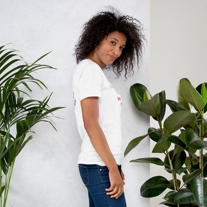 Woman wearing a white t-shirt with a 'Fun Wear Code' text logo and colorful texts, standing between two potted plants against a light gray wall.